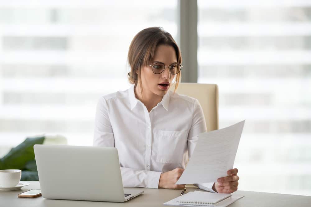 amazed woman office worker feeling stunned baffled by unbelievable information in paper about debt or dismissal