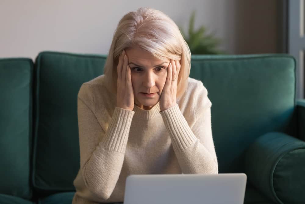 surprised senior old lady looking at laptop amazed by unexpected stuck computer problem sit on sofa at home
