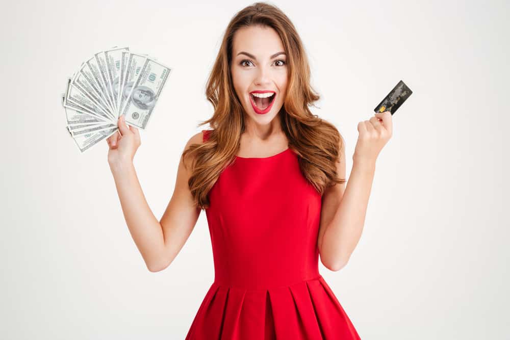 Closeup portrait smiling woman in red dress with credit cards in one hand and cash in other isolated on a white background